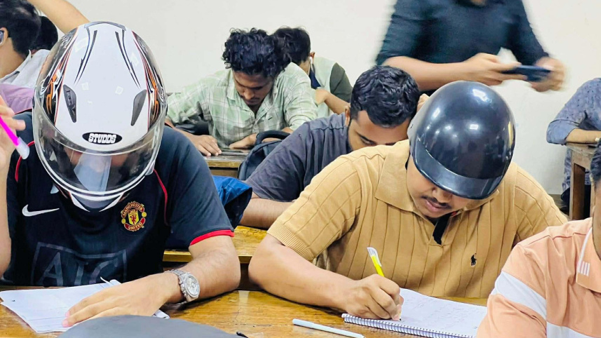 ছাদ থেকে খসে পড়ে পলেস্তারা, তাই হেলমেট পরে পরীক্ষা দিচ্ছেন শিক্ষার্থীরা। ছবি: স্টার