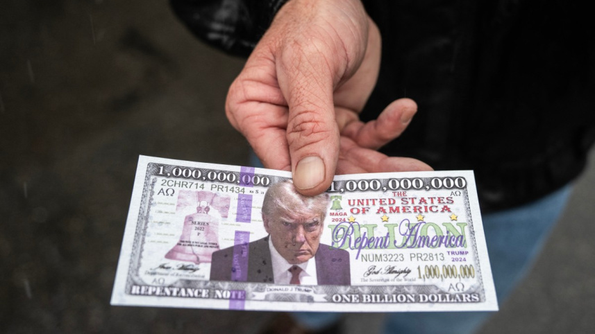 ট্রাম্পের ছবি ও বাইবেলের উক্তি সম্বলিত 'ভুয়া' ডলার বিতরণ করছেন এক ট্রাম্প সমর্থক। ছবি: এএফপি