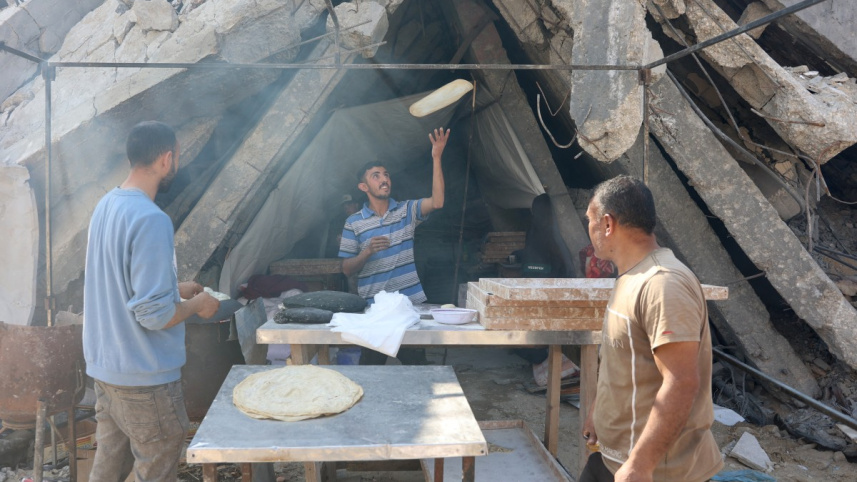 যুদ্ধবিরতি চলাকালীন উত্তর গাজার জাবালিয়ায় ধ্বংস হয়ে যাওয়া বাড়ির সামনে রুটি বানাচ্ছেন এক ফিলিস্তিনি। ছবি: এএফপি 