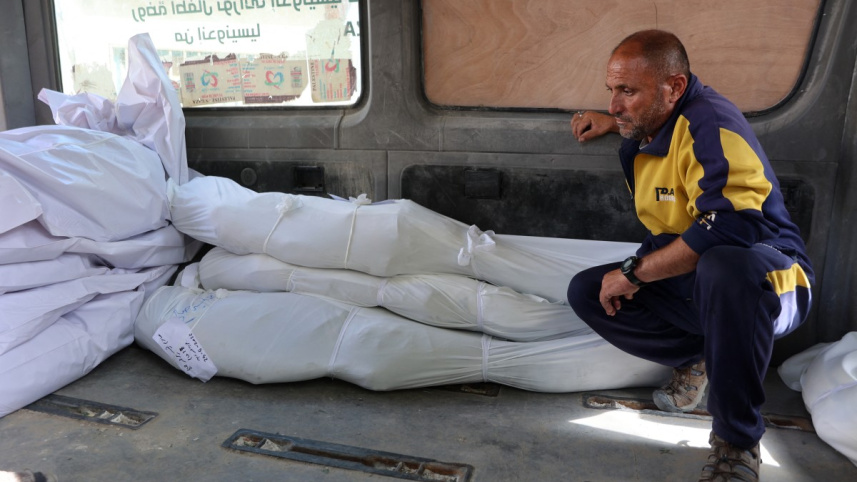 নিহত স্বজন-প্রতিবেশীদের মরদেহের সামনে বসে আছেন এক ফিলিস্তিনি। ছবি: এএফপি