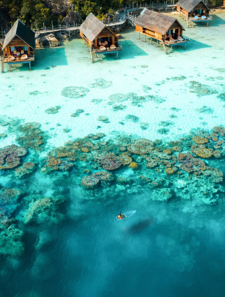 aerial-man-holding-oar-clear-kayaking-coral-reefs-lagoon-from-distance-west-overwater-suite